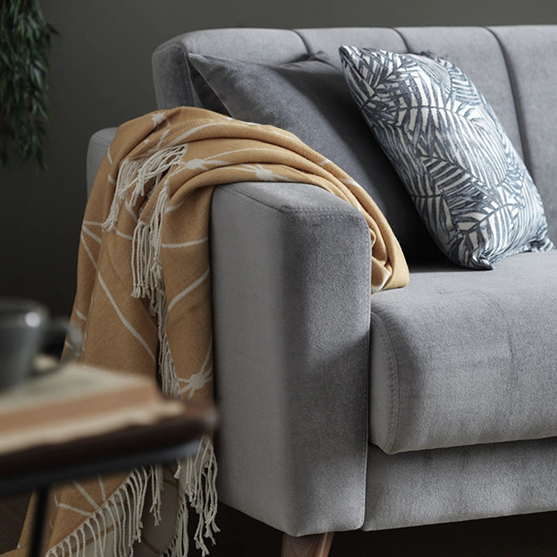 Gray sofa with a beige throw blanket and a patterned pillow, next to a wooden side table.