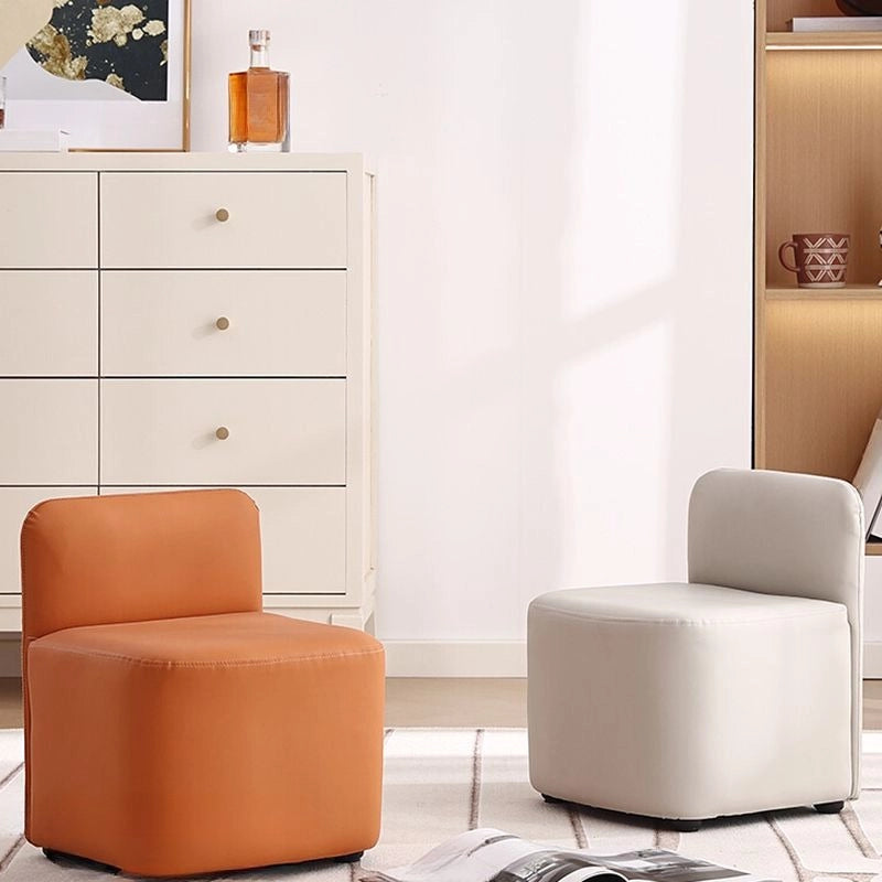The Europa pouffe chair features a low-rise backrest, foam-filled cushioning, and smooth leatherette upholstery in a choice of vibrant solids—ivory, orange 