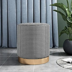 Patterned ottoman with gold base in a room setting with curtains and plant